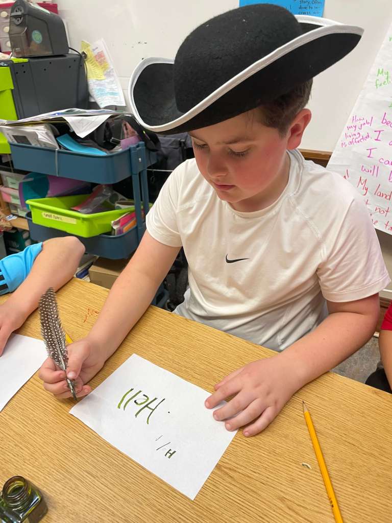 a child in a tri-corn hat writing with a quill