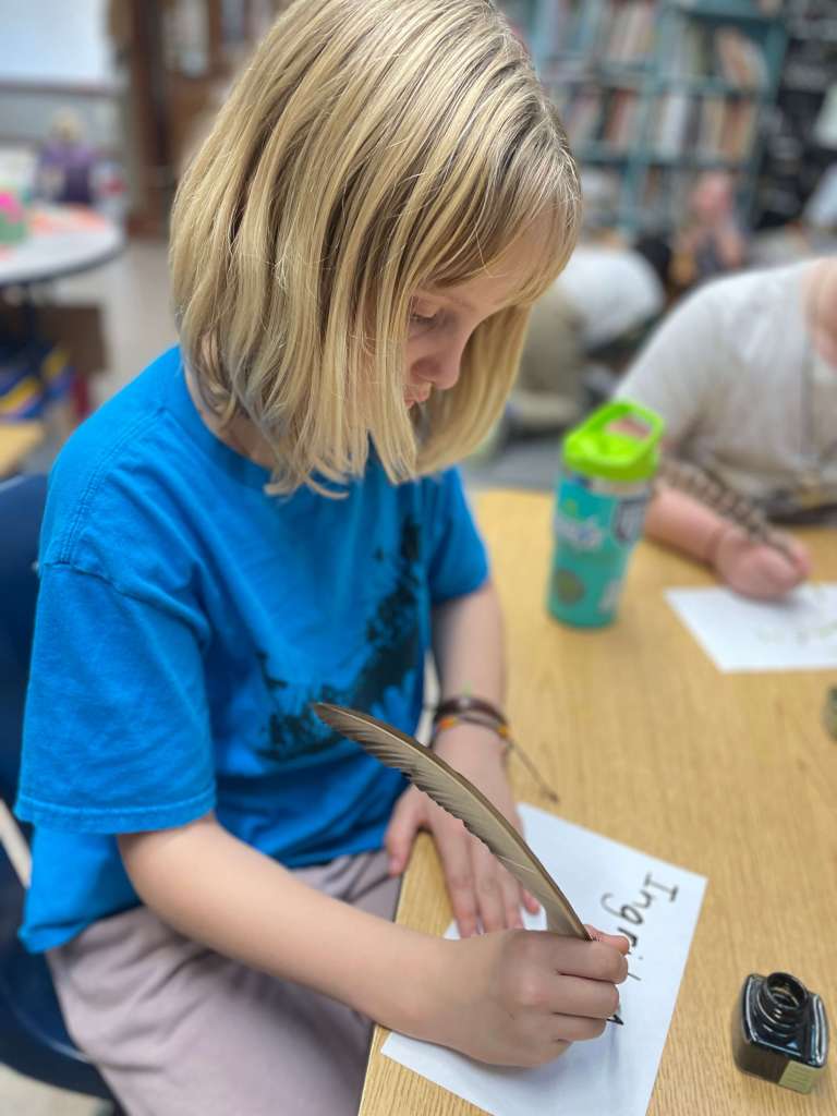 a child in a blue shirt writing with a quill