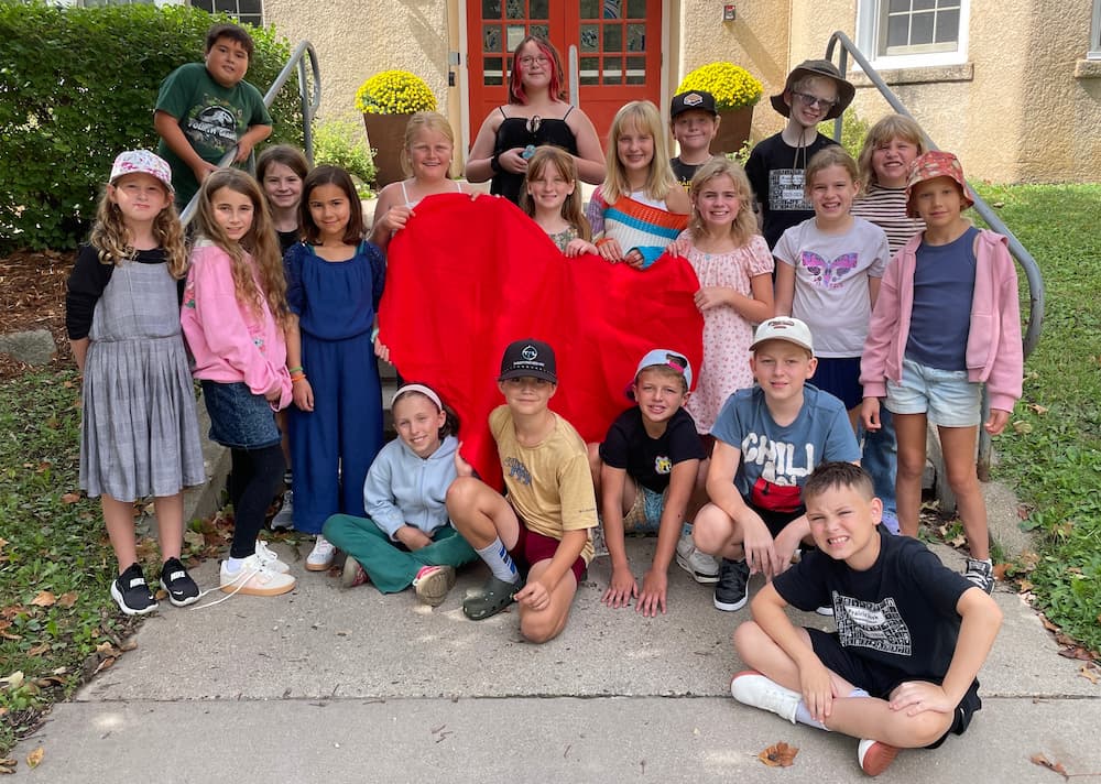 Group of elementary age students holding a felt heart in front of a school